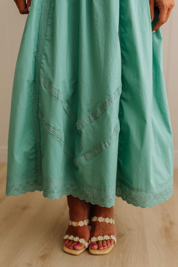 Teal dress with lace details worn by a person on a wooden floor.
