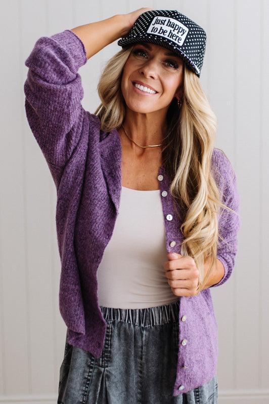 BLONDE WOMAN WEARING A COZY RIBBED TEXTURE CARDIGAN WITH SHELL BUTTONS AND A POLKA DOT HAT.