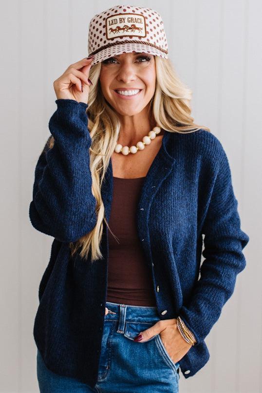 BLONDE WOMAN WEARING A COZY RIBBED TEXTURE CARDIGAN WITH SHELL BUTTONS AND A POLKA DOT HAT.