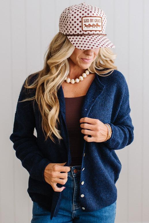 BLONDE WOMAN WEARING A COZY RIBBED TEXTURE CARDIGAN WITH SHELL BUTTONS AND A POLKA DOT HAT.