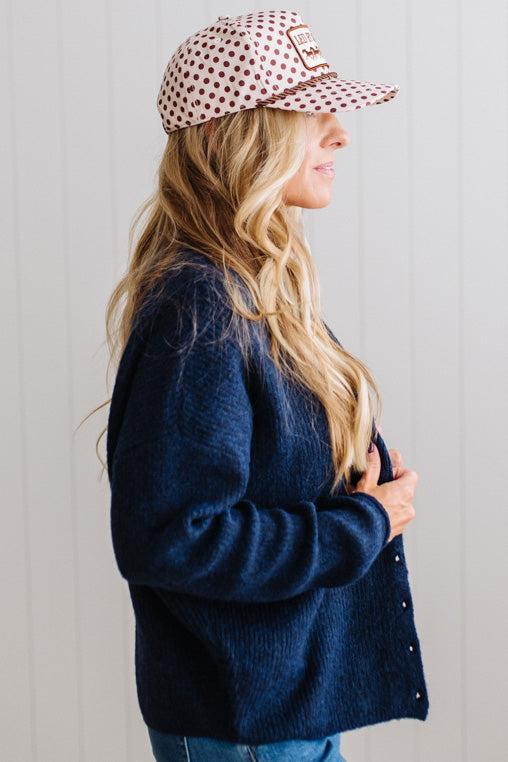 BLONDE WOMAN WEARING A COZY RIBBED TEXTURE CARDIGAN WITH SHELL BUTTONS AND A POLKA DOT HAT.