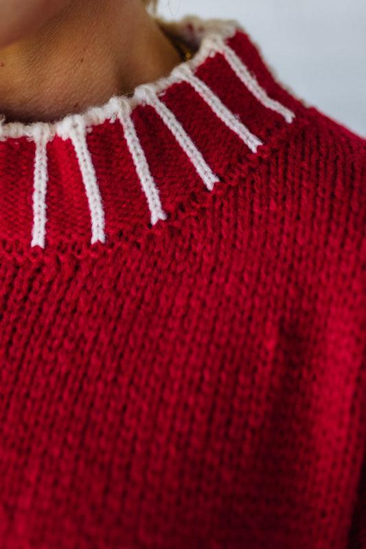 Close-up of a red sweater with white trim on a plain background