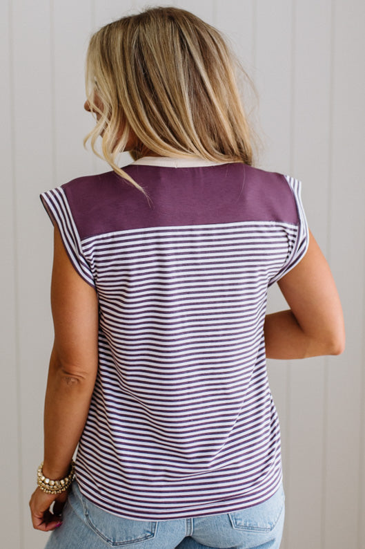 Woman wearing a striped shirt with a purple top and white stripes, standing against a plain background.
