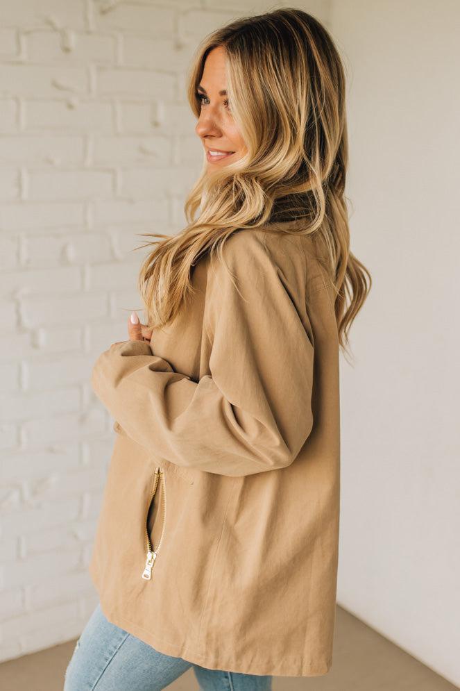 Woman wearing a beige jacket against a white brick wall
