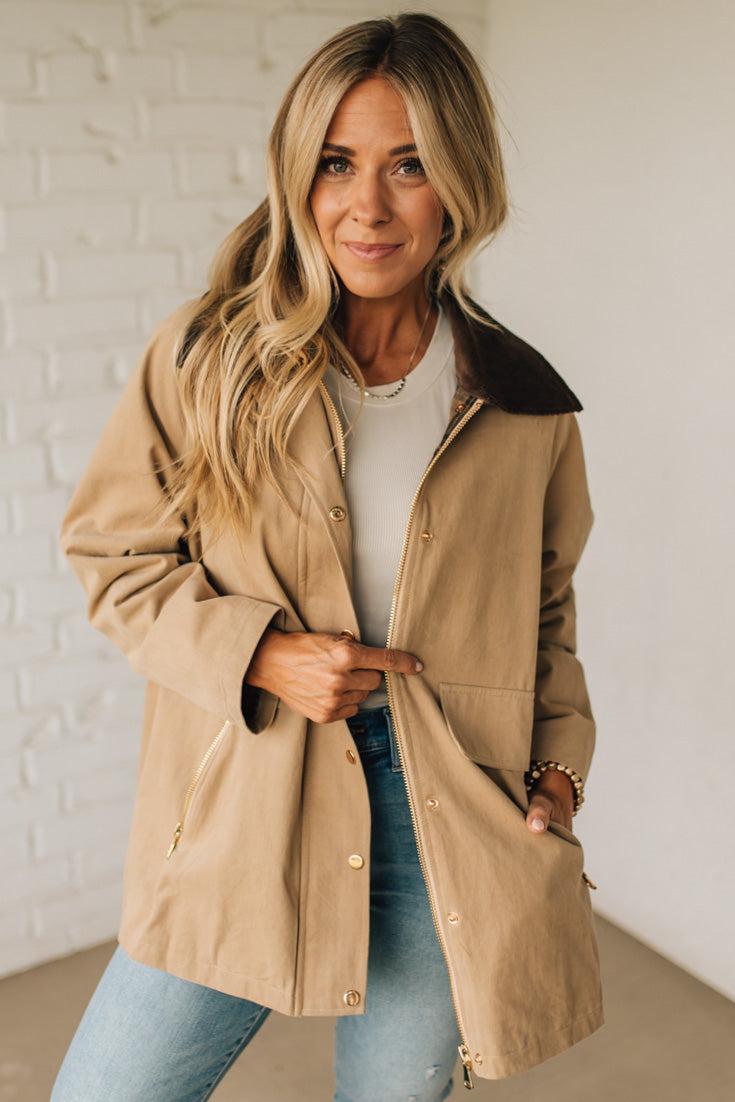 Woman wearing a beige coat with a white brick wall background