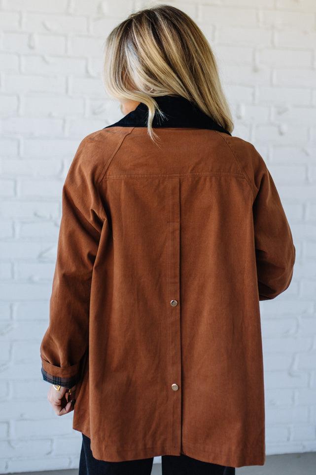 Person wearing a brown jacket with a white brick wall background