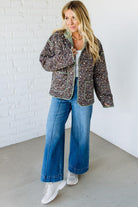 Woman wearing a patterned jacket, white shirt, blue jeans, and white sneakers against a white brick wall.