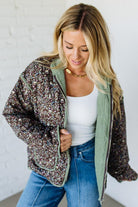 Woman wearing a floral jacket over a white top and blue jeans against a white wall.