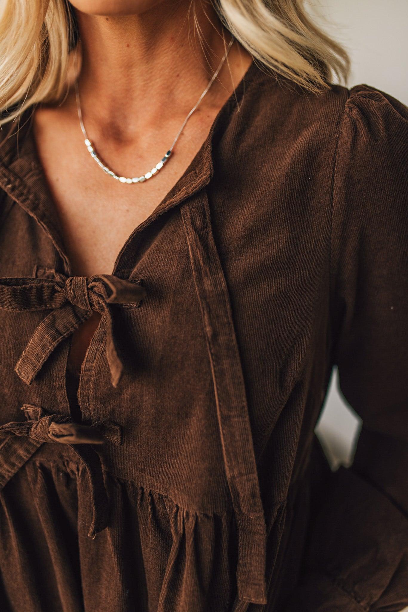 Brown dress with a close-up of a necklace worn by a person.