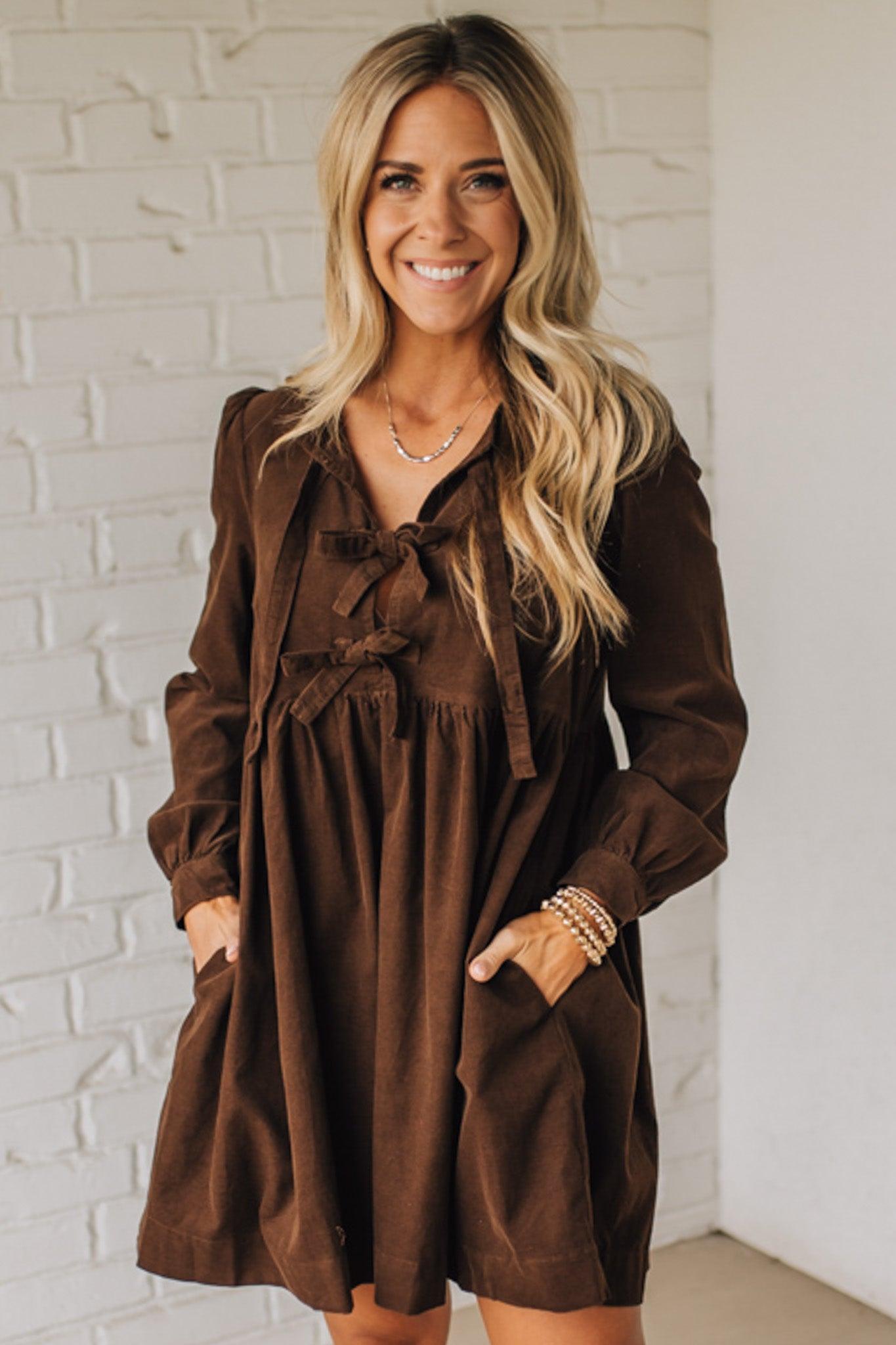 Woman wearing a brown dress against a white brick wall