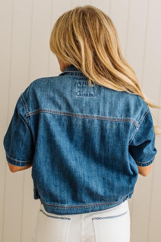 Person wearing a blue denim jacket from behind with a neutral background