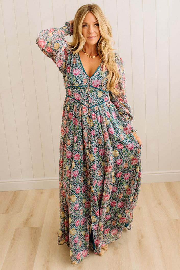 Woman wearing a floral dress against a light wooden paneled wall.