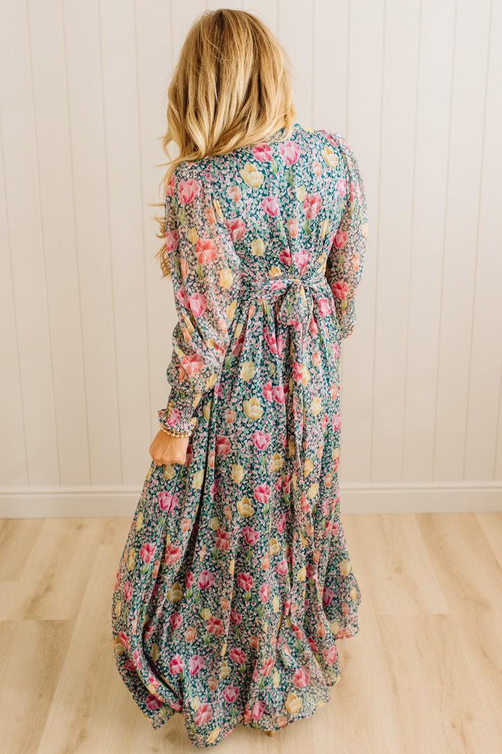 Woman wearing a floral dress standing against a wooden paneled wall.