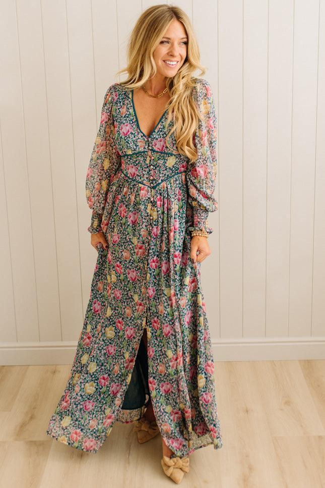 Woman wearing a floral dress standing against a white paneled wall.