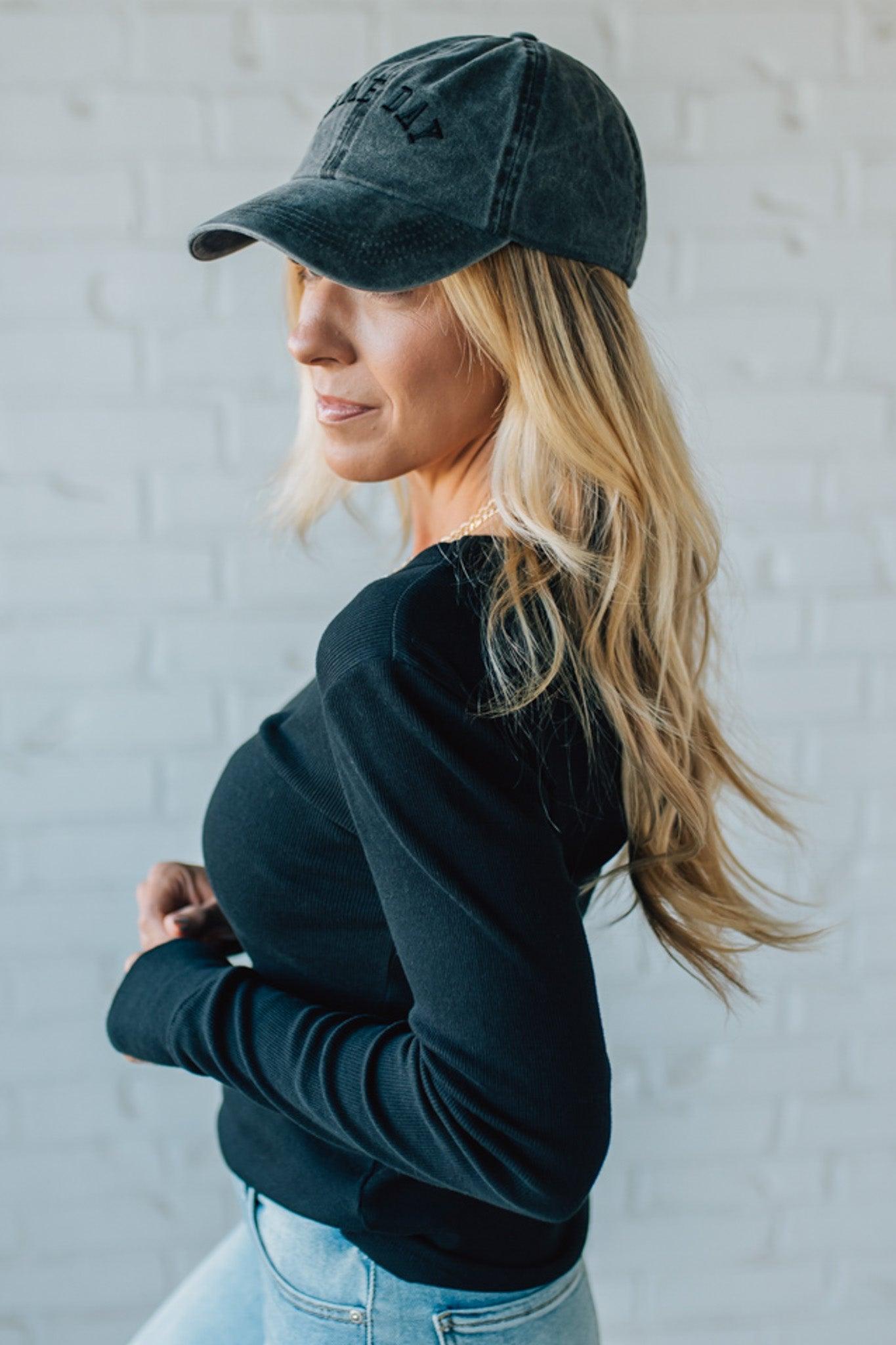 Woman wearing a black cap and black long-sleeve shirt against a white wall