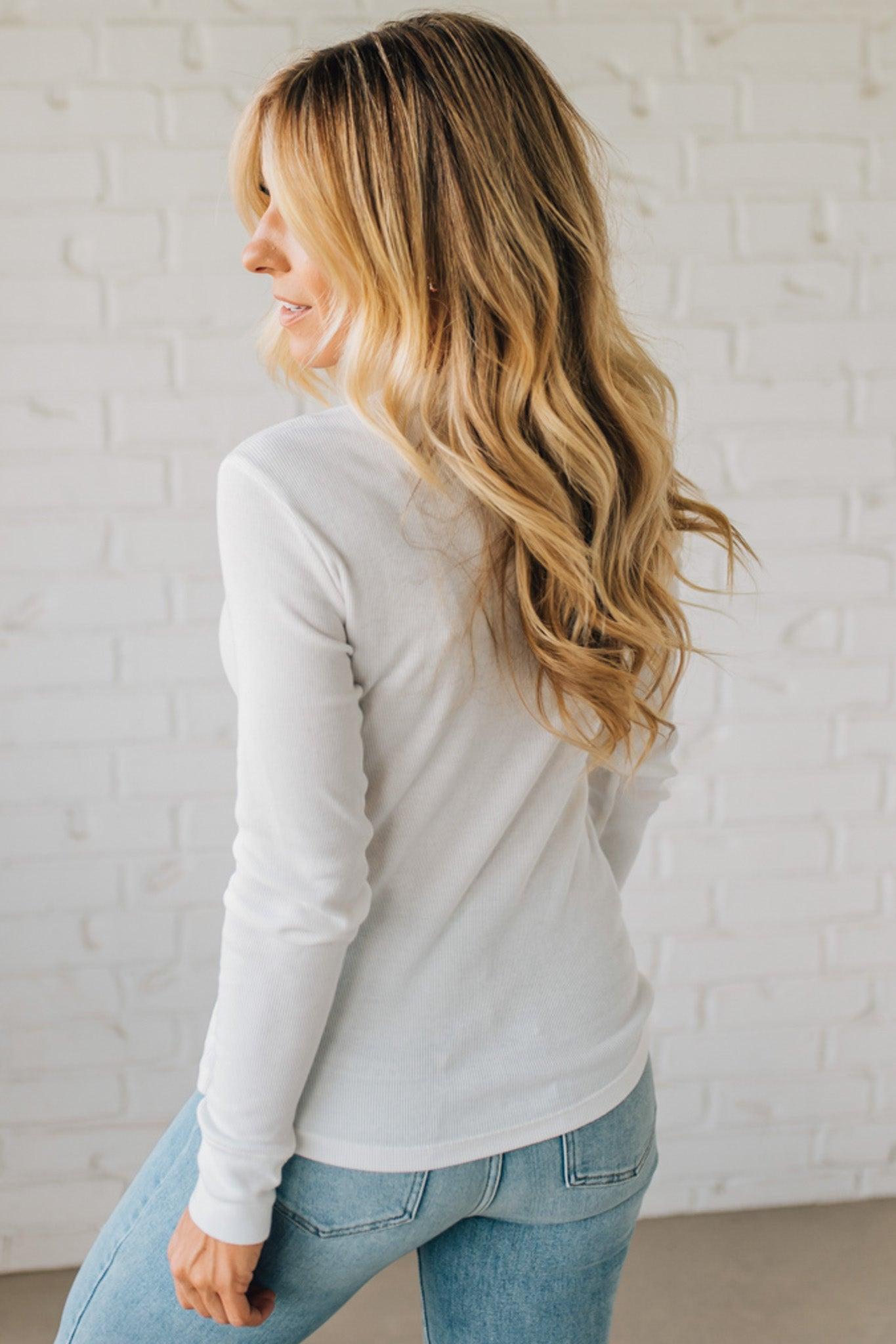 Woman wearing a light gray sweatshirt and blue jeans against a white brick wall.