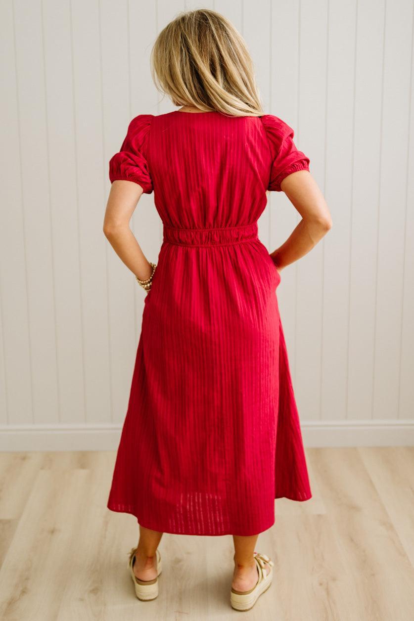 Woman wearing a red dress standing against a white paneled wall.