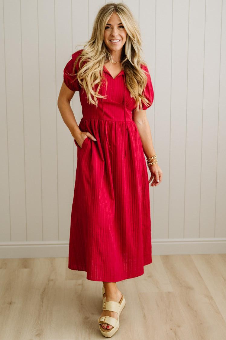 Woman wearing a red dress standing against a white paneled wall.