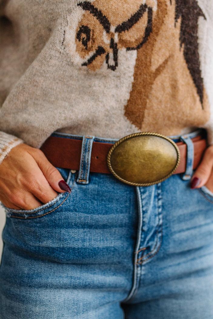 Close up image of a woman in blue jeans and patterned sweater featuring a Western Oval Buckle Leather Belt.