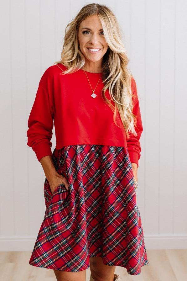 Blonde woman wearing a knee length dress with red french terry top, and red plaid skirt bottom with pockets on the sides.