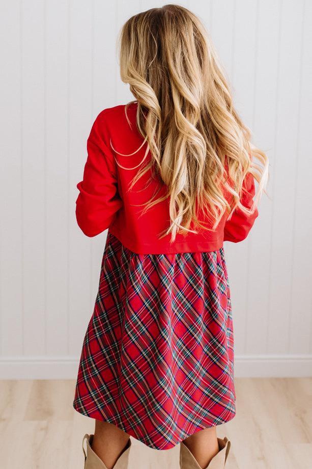 Blonde woman wearing a knee length dress with red french terry top, and red plaid skirt bottom with pockets on the sides.