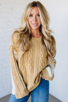 Woman wearing a beige cable knit sweater with white lining against a white background