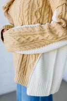 Close-up of a person wearing a beige cable knit sweater with white lining.