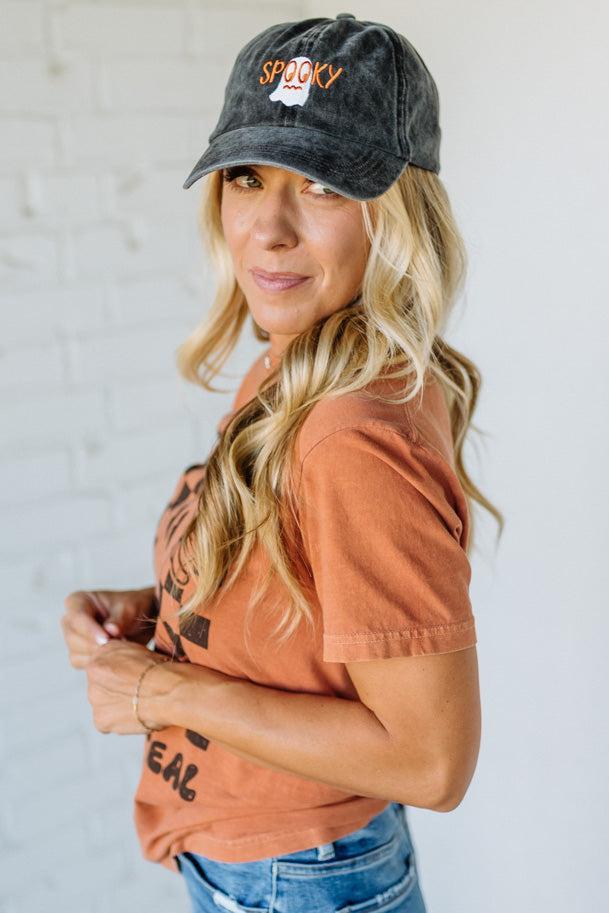 Woman wearing a black cap with 'Spooky' text and an orange shirt against a white background