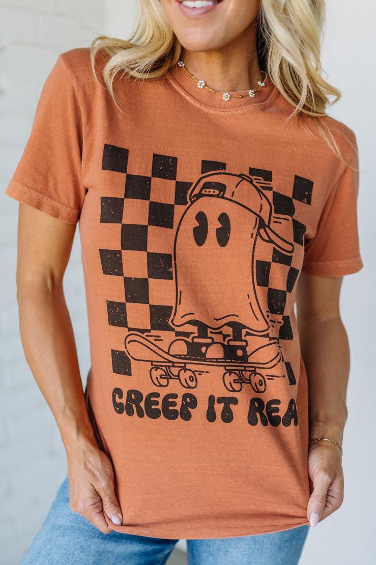 Person wearing a brown t-shirt with a graphic design and text.