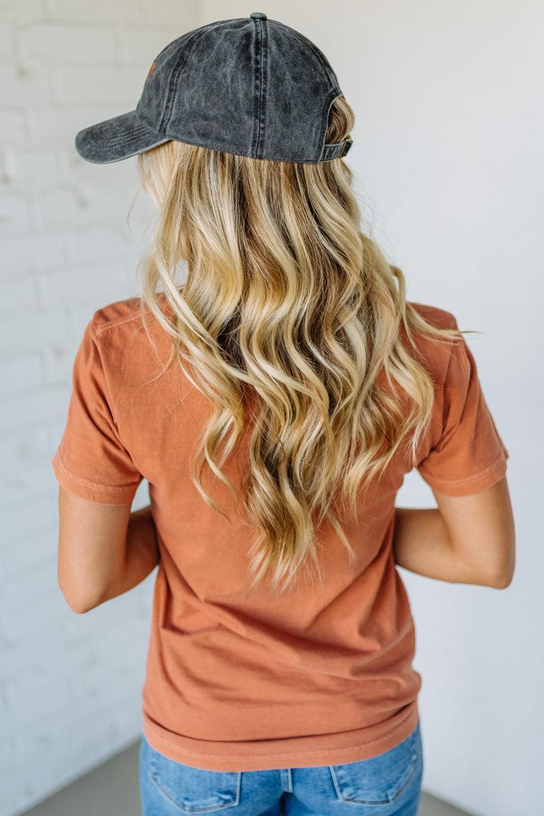 Person wearing a denim cap and orange shirt with blonde hair against a white background