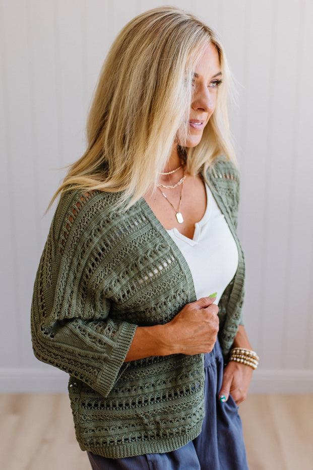 Woman wearing a green knitted cardigan over a white top, standing against a plain background.