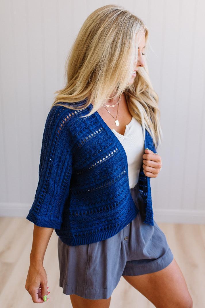 Woman wearing a blue knitted cardigan over a white top and gray shorts.