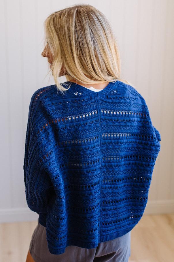 Person wearing a blue crocheted sweater with a neutral background