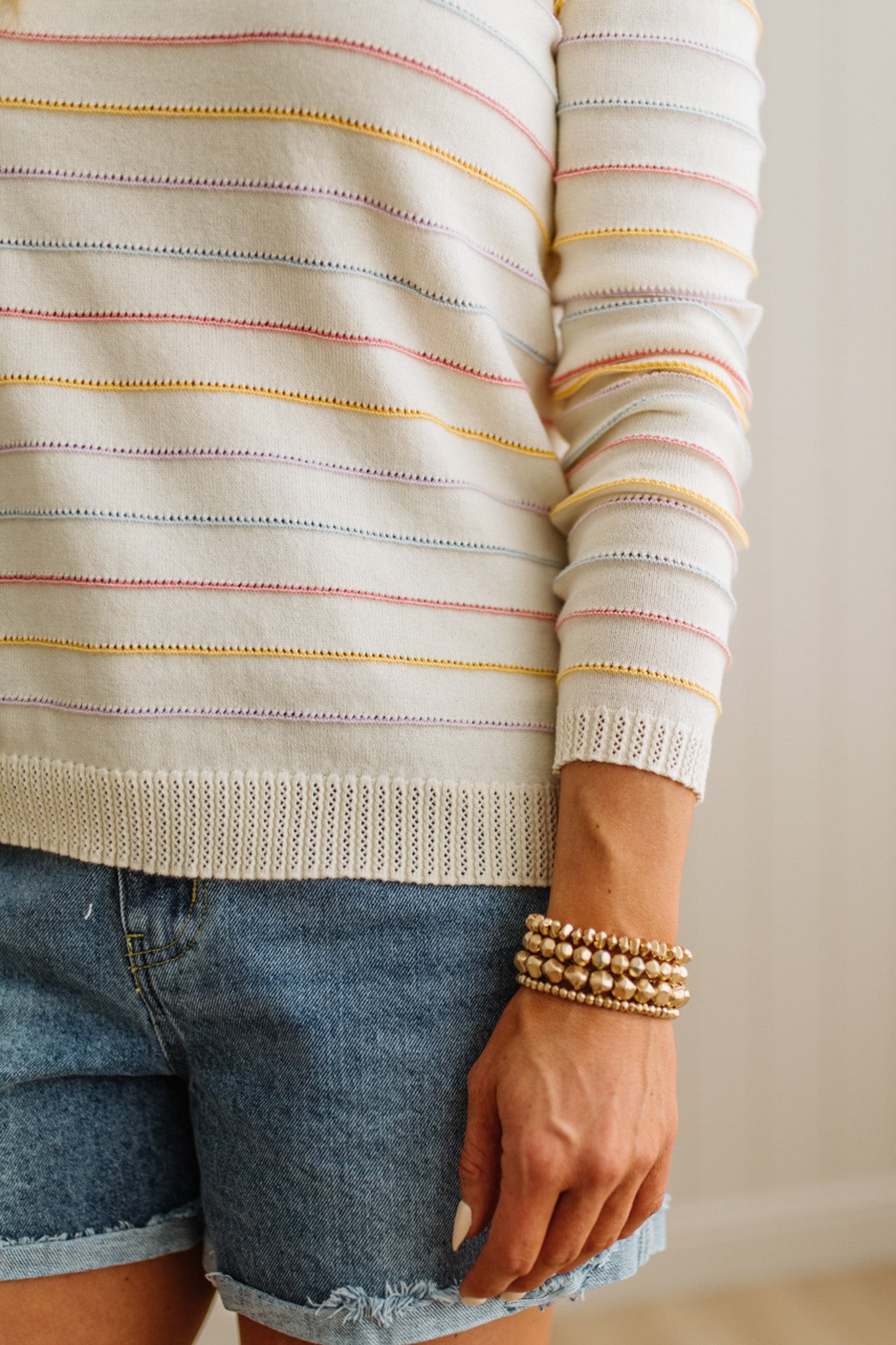 Person wearing a striped sweater and denim shorts with a plain background