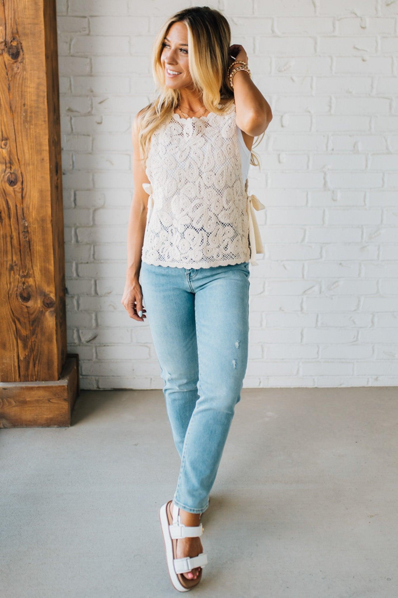 BLONDE WOMAN WEARING A FLORAL CROCHET VEST TOP WITH OPEN SIDES WITH TWILL TAPE TIE.