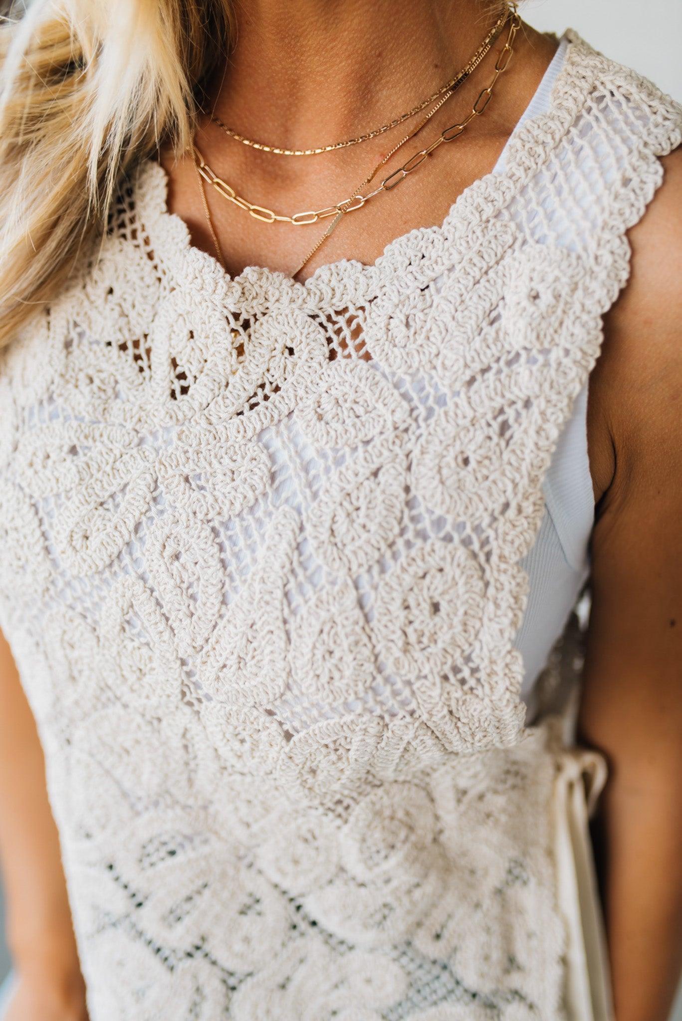 BLONDE WOMAN WEARING A FLORAL CROCHET VEST TOP WITH OPEN SIDES WITH TWILL TAPE TIE.