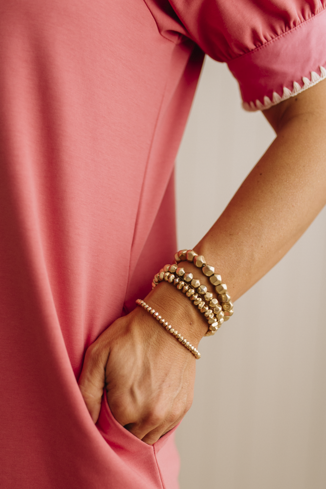 Person wearing a pink outfit with gold bracelets on a neutral background