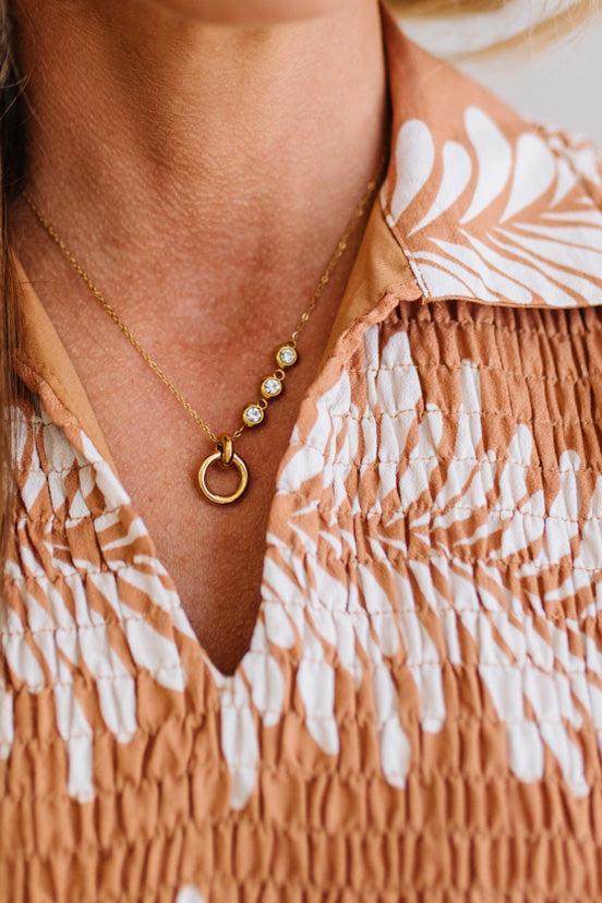 Close-up of a person wearing a gold necklace with circular pendants on a patterned garment.