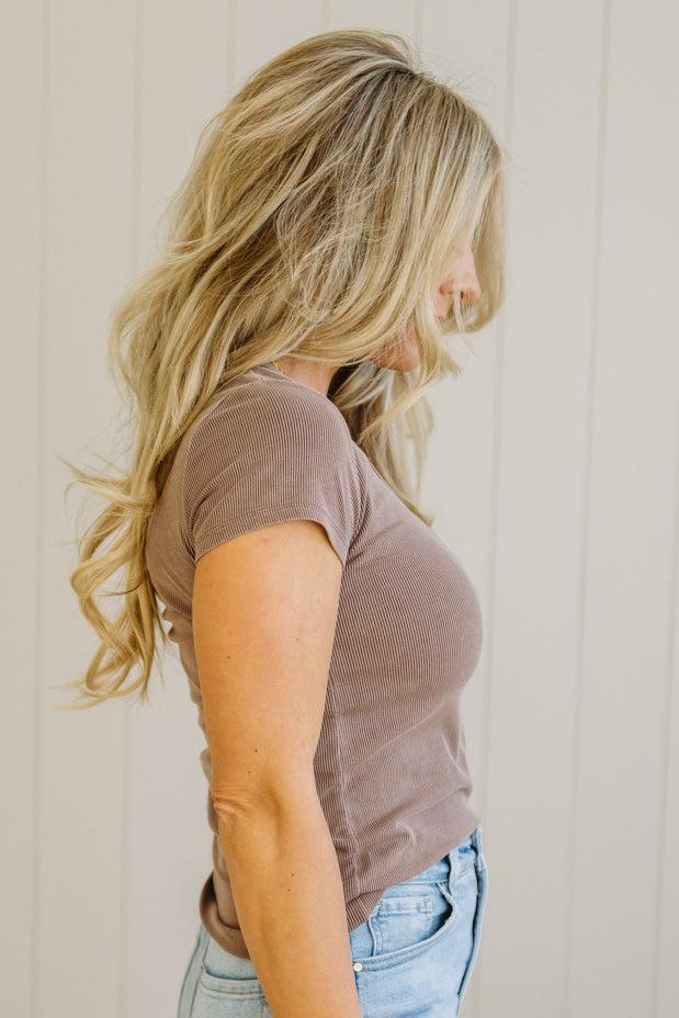 Woman wearing a brown t-shirt and blue jeans against a plain background