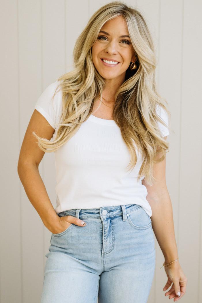 Woman wearing a white t-shirt and light blue jeans against a neutral background