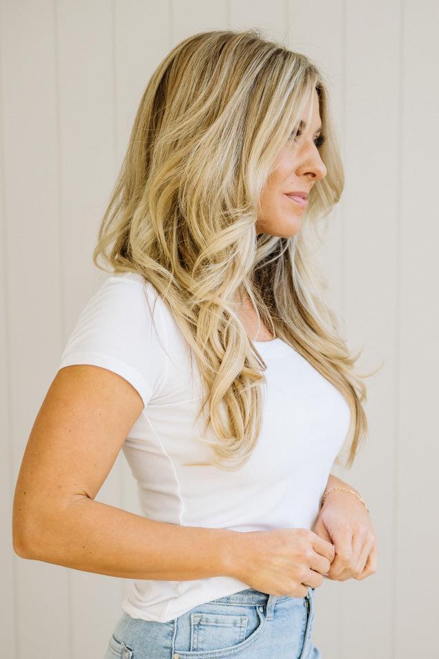 Woman with long blonde hair wearing a white t-shirt and blue jeans against a neutral background