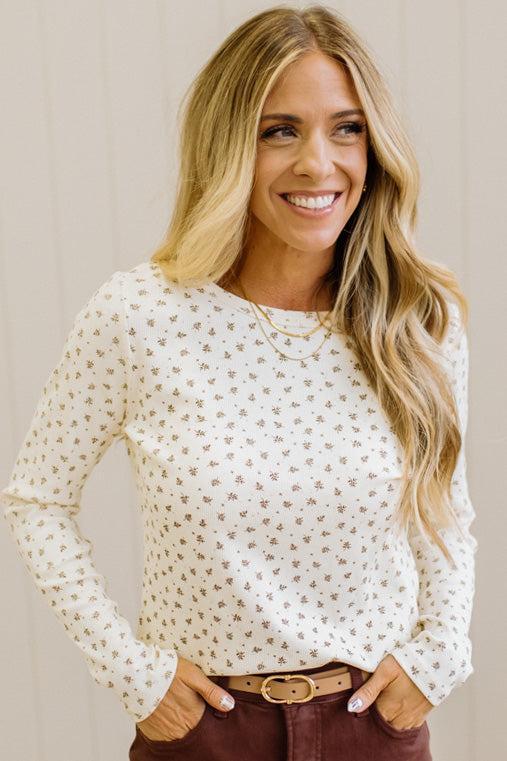 Blonde woman in brown jeans wearing a cream long sleeve tee with brown botanical print.