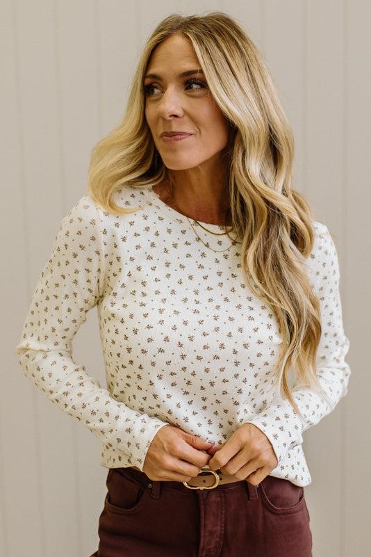 Blonde woman in brown jeans wearing a cream long sleeve tee with brown botanical print.