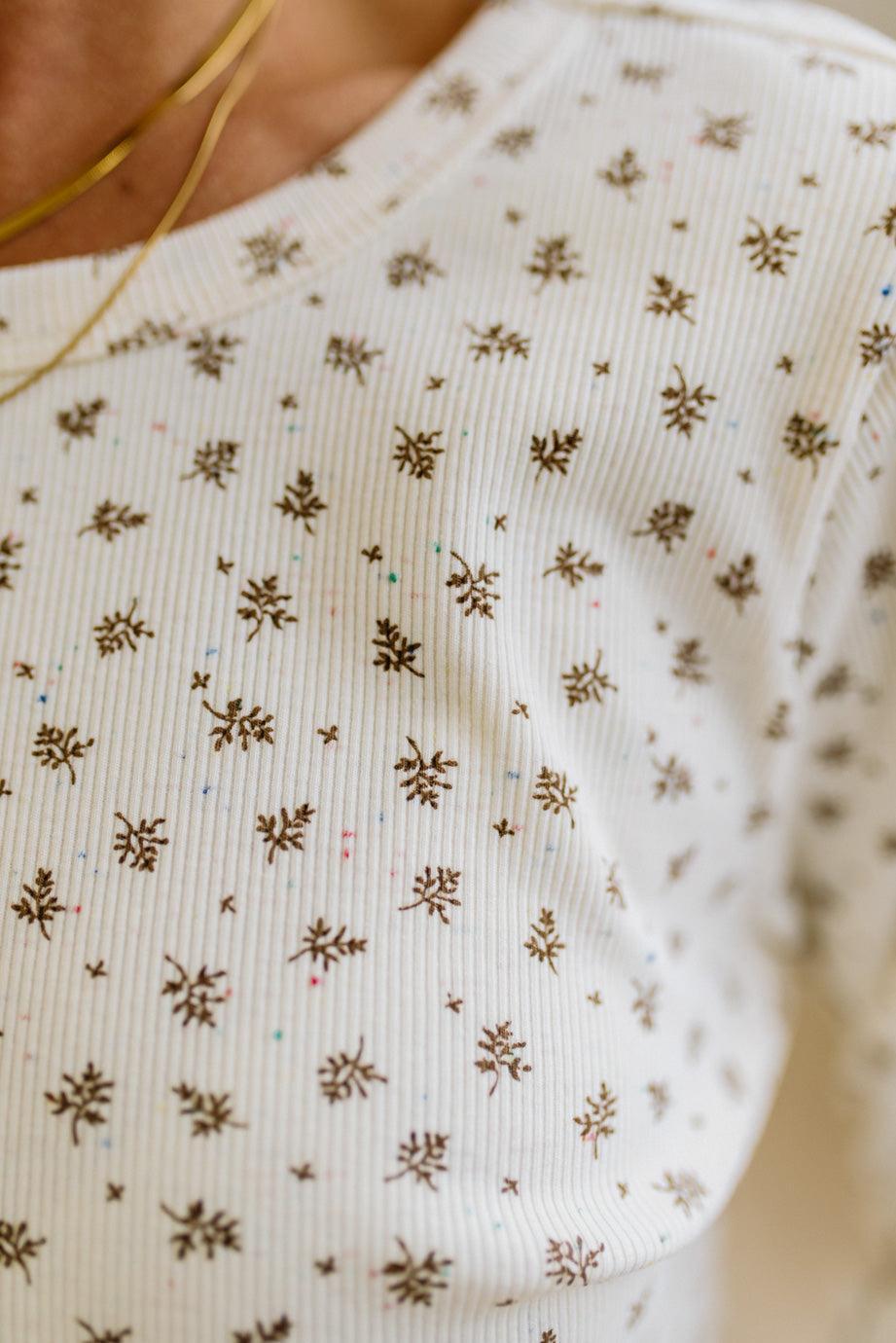Blonde woman in brown jeans wearing a cream long sleeve tee with brown botanical print.