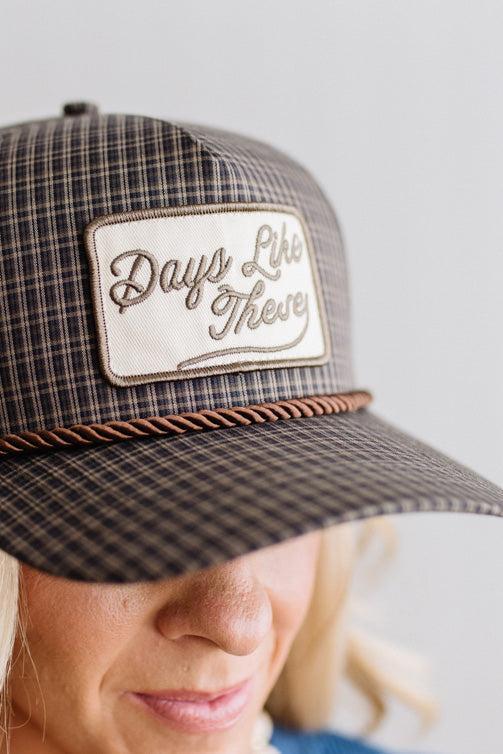 Blonde smiling woman wearing a plaid hat with a brown rope across the front, and a patch that is cream with brown embroidery that says Days Like These.