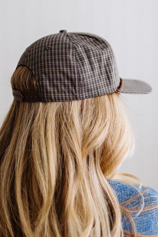 Blonde smiling woman wearing a plaid hat with a brown rope across the front, and a patch that is cream with brown embroidery that says Days Like These.