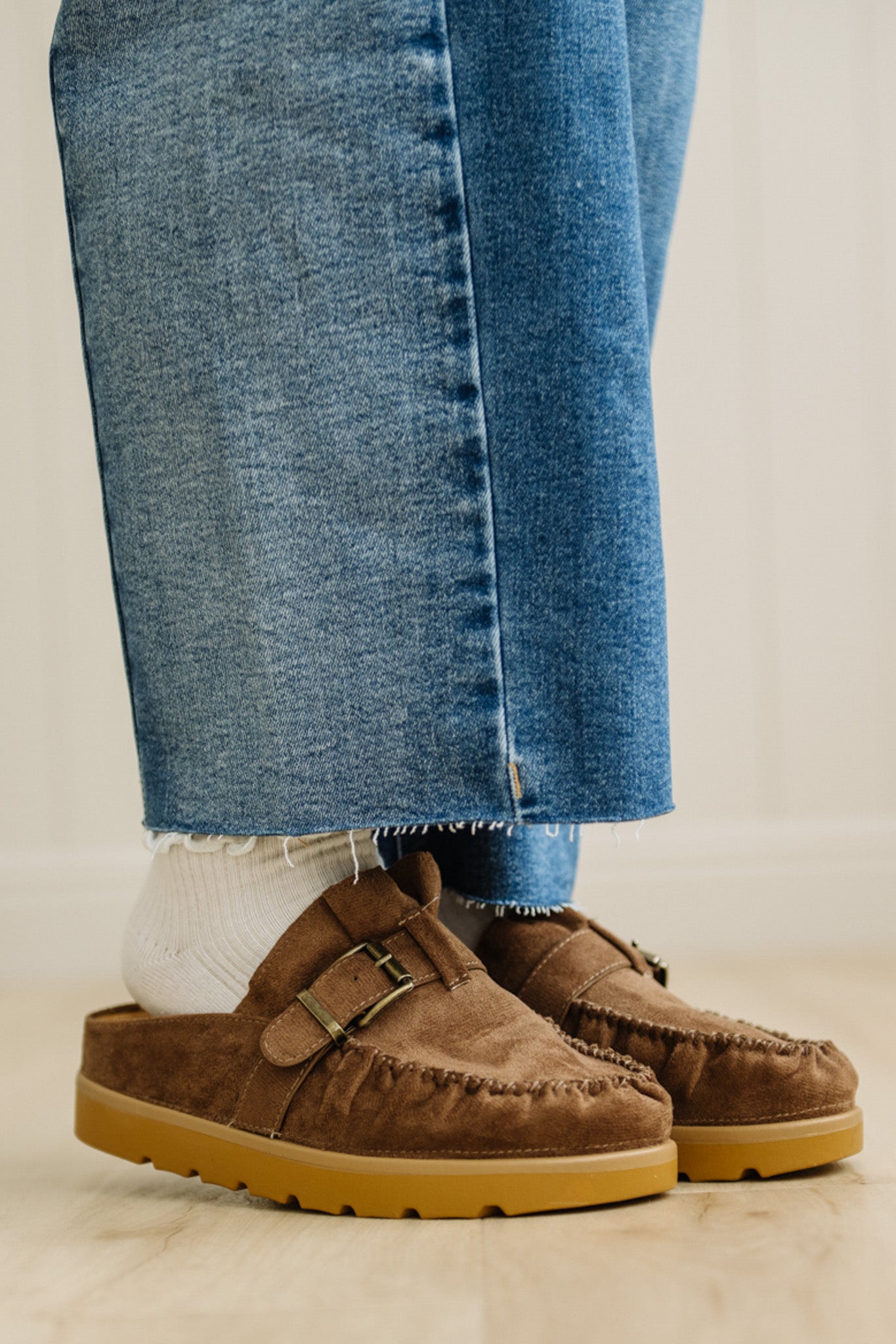 Brown suede shoes with buckles worn with blue jeans on a neutral background