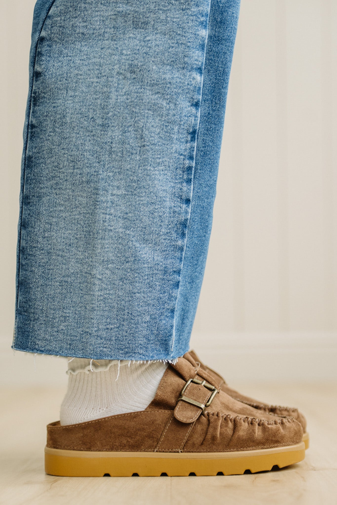 Brown suede shoes with tan soles worn with blue jeans on a neutral background