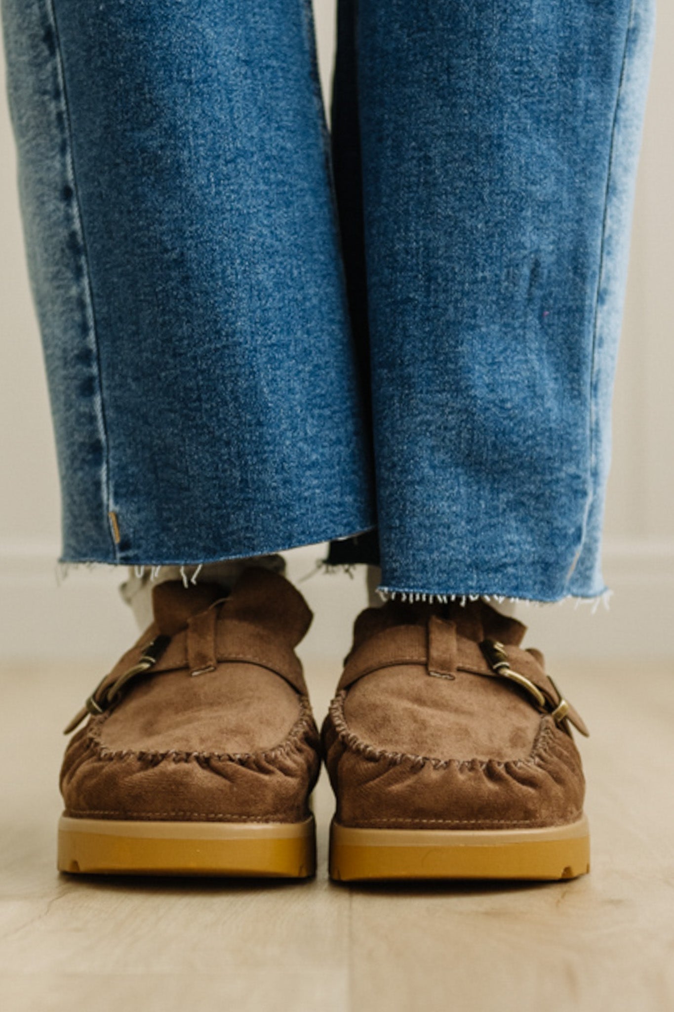 Brown suede loafers worn with blue jeans on a light background
