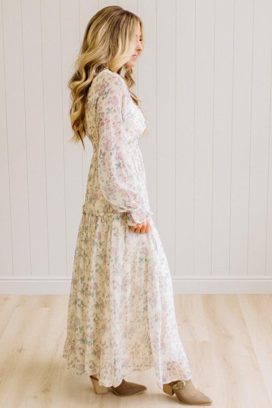 Woman wearing a cream floral dress against a white paneled wall.